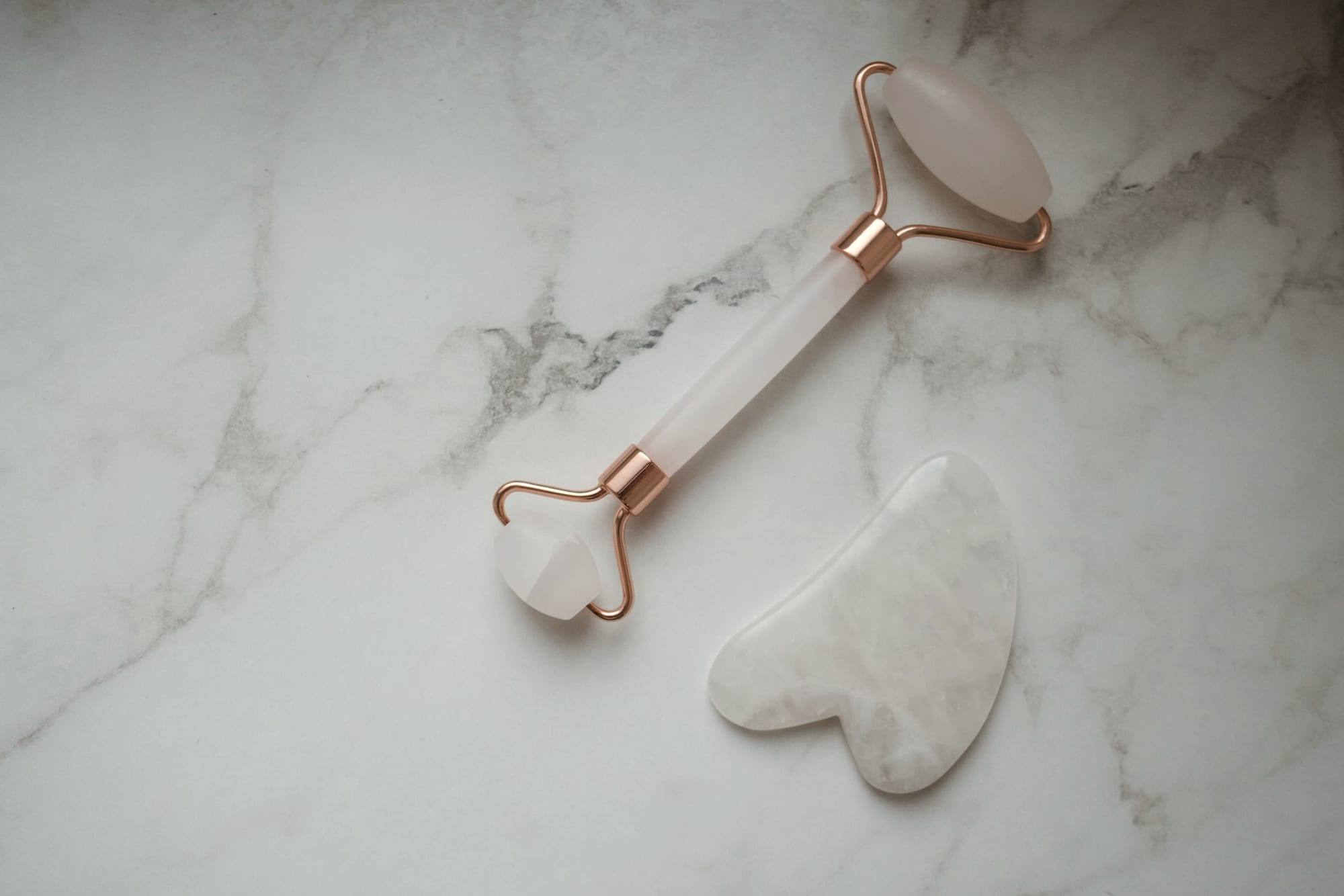 Açık mermer üstünde yüz masaj rulosu ve gua sha taşı